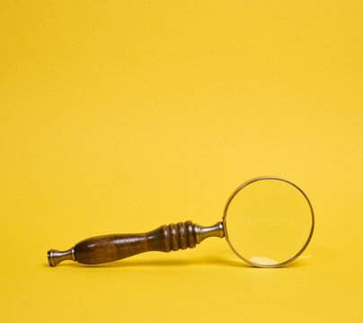 A vintage magnifying glass with a wooden handle lying on a yellow background.