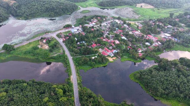 Aerial view of a small village by lakes. Green forests surround the settlement at Tasik Raban