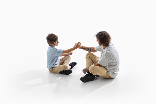 Father and son sit facing each other and share friendly handshake. Family teamwork, mutual understanding and positive parenting concept.