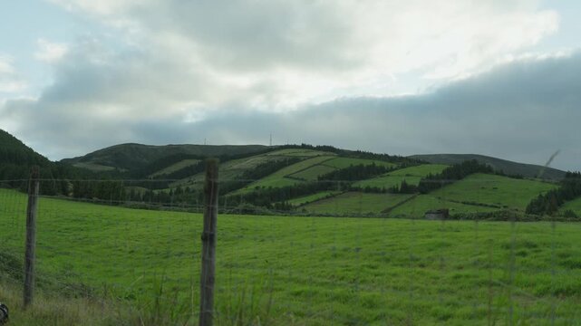 Wooden fence posts border a green pasture, with patchwork fields and hedgerows on rolling hills behind, on Sao Miguel island.