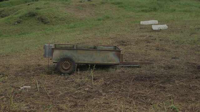 An old rusty farm trailer stands on trampled grass in a hillside pasture on Sao Miguel island in the Azores.