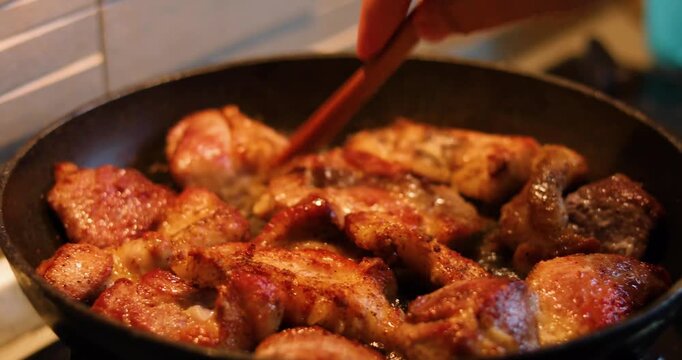 Close-up of pork pieces being fried and flipped in a frying pan for dinner