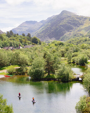Paddleboarders on calm green waters of Llyn Peris with dramatic Snowdonia mountain peaks in the background, Llanberis, North Wales