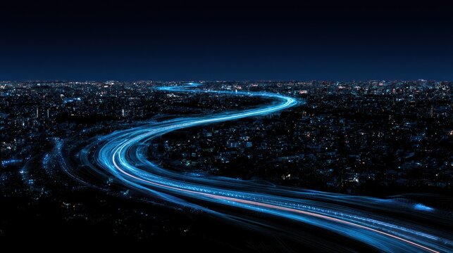 Aerial view of a winding highway with blue light streaks at night over a cityscape