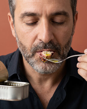 Contemplative man savors a forkful of canned fish, eyes closed against a bold color backdrop
