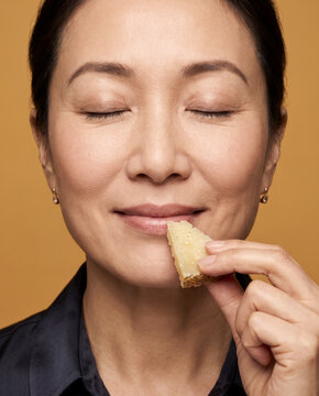 Serene woman savors a bite of cheese, with closed eyes in soft beauty lighting