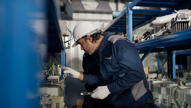 Maintenance technician inspects robotic arm spare parts and electronic components in industrial warehouse, supporting inventory control, identification, repair planning, reliability, efficiency.