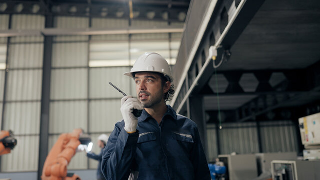 Male robotic technician walking patrol and communication with team speaks walkie-talkie in robot warehouse.