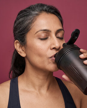 Focused woman drinks a protein shake from a shaker bottle, with closed eyes