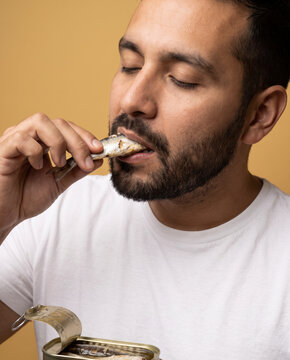 Weathered man eats preserved seafood from a tin by hand, with closed eyes