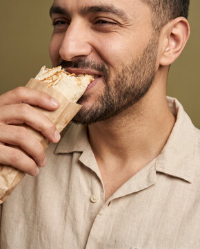 Hearty man bites into a large wrap sandwich, with a grin in soft beauty lighting