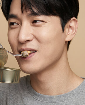 Weathered man eats preserved food from a tin with a fork, and a satisfied gaze