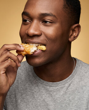 Hearty man bites a savory fish and chips by hand, with appetite against a bold color backdrop