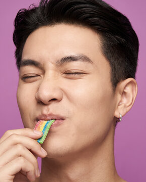 Playful man bites colorful candy, with closed eyes against a bold color backdrop