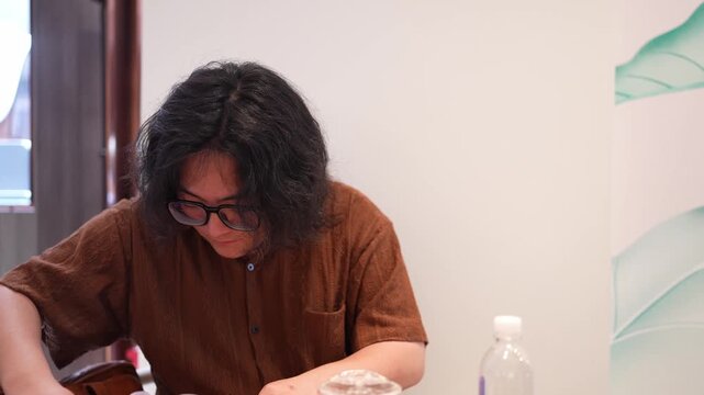 A seated man looks down and handles a small translucent pouch on the cafe table.