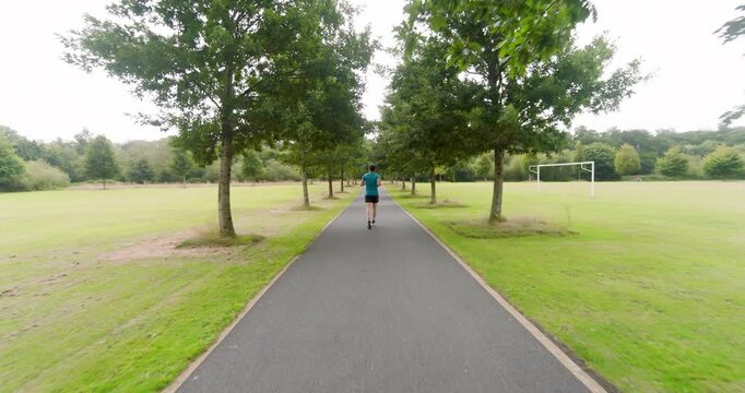 Person jogging on scenic park path surrounded by lush green trees