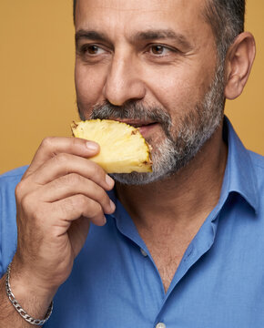 Tropical man bites a chunk of fresh pineapple, with a smile in a tight, expressive crop