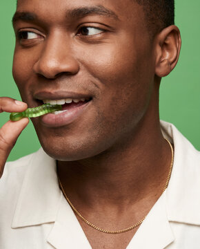 Fresh man bites a green gummy worm, with a smile with warm, saturated color