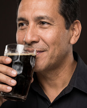 Relaxed man drinks a dark stout beer, with satisfaction with striking studio color