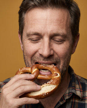 Rustic man bites a soft pretzel, with both hands with striking studio color