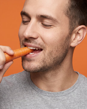Fresh man bites a fresh carrot, with closed eyes with striking studio color