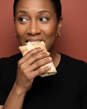 Hearty woman bites a savory stuffed wrap, with closed eyes against a bold color backdrop