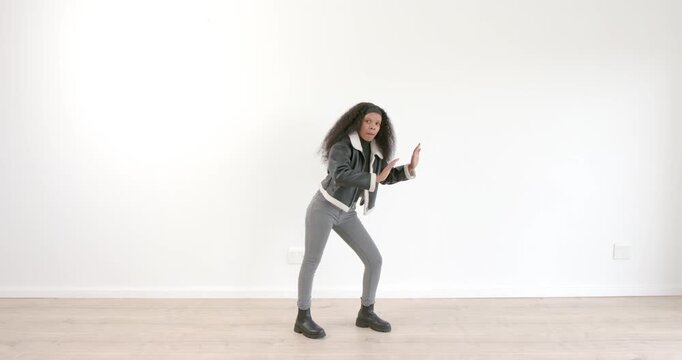 Young woman dancing energetically in casual outfit on wooden floor indoors