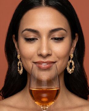Refined woman sips a glass of white wine, gracefully against a solid studio background