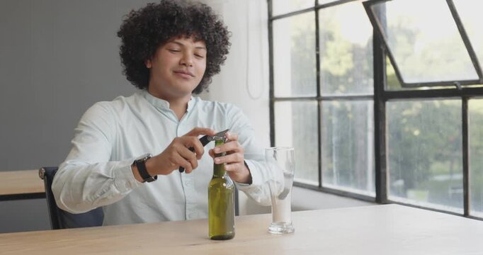 Smiling man pouring beer into glass at office desk during break
