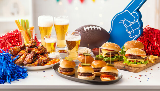 Game Day Party Spread with Glazed Chicken Wings Mini Sliders Cheeseburgers and Cold Lager Beer on White Table with Football and Foam Finger