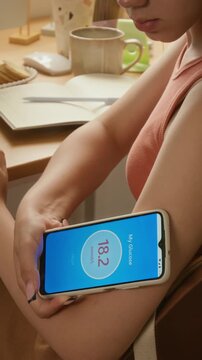 Vertical video of biracial young girl scanning glucose sensor on arm using smartphone and logging data in notebook. Ideal for modern diabetes management, medical technology and healthcare ads