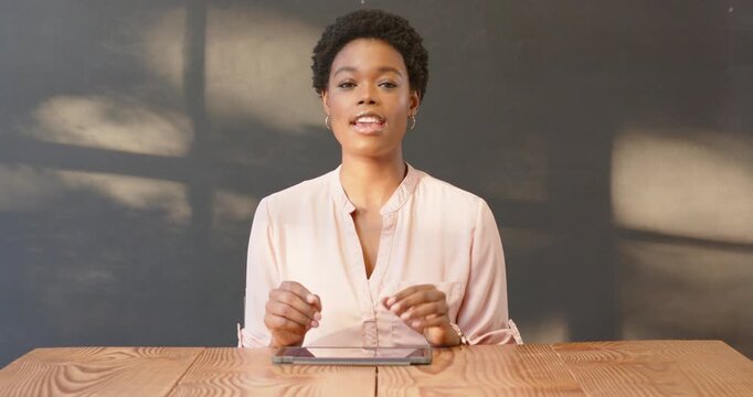 African American woman using tablet at office desk, engaged in virtual meeting