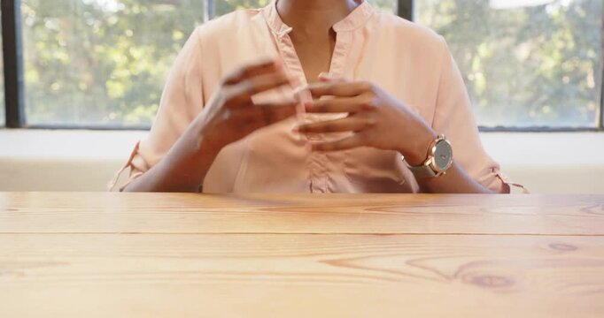 African American woman sitting at table, wearing watch, hands resting together
