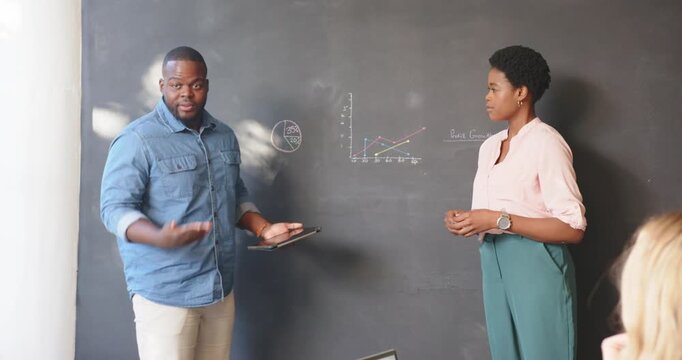 Business professionals discussing and presenting charts on chalkboard in office meeting while holdin