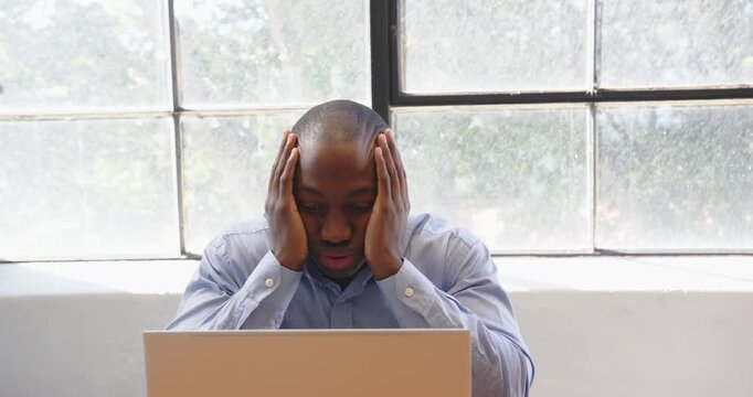 African American man in office thinking deeply while working on laptop