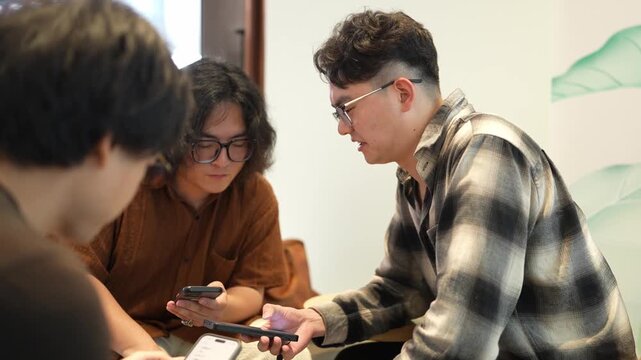 Two men lean forward and look closely at smartphones while seated together indoors.