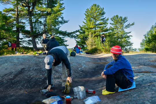 Two expedition participants clean up camp kitchen gear after breakfast on granite campsite under pine trees on Georgian Bay, Ontario, Canada
