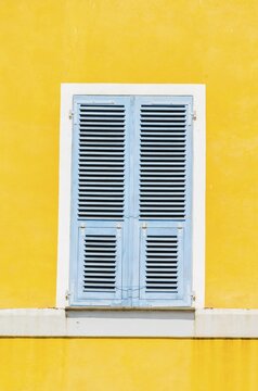 Yellow plastered wall with closed bright blue wooden shutters, Corsica, France