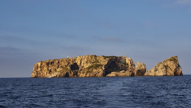 A rocky island rises from the blue sea, shining under a clear sky, morning light, Tsichli Babas islet, Navarino Bay, Pylos, Peloponnese, Greece