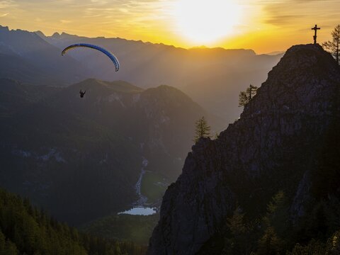 Paraglider flying next to the summit cross of the small Jenner at sunset, Reiteralpe in the background, Berchtesgaden National Park, Sch&ouml;nau am K&ouml;nigssee, Upper Bavaria, Bavaria, Germany