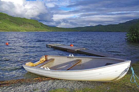 A rowing boat is moored on a small jetty on a quiet lake, surrounded by mountains, Sjak, Valdesflyra, Norway