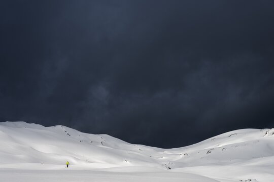 Ski tourer on a vast plateau with snow-covered mountains in the background and dramatic sky, Berlinger K&ouml;pfle, Ritzlern Kleinwalsertal, Vorarlberg, Austria
