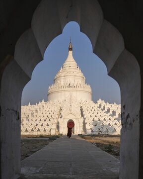 Buddhist monk stands with red umbrella in front of Hsinbyume Pagoda with frame of another pagoda, Mingun, Myanmar