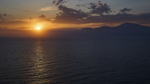 Sunset behind clouds over sea with mountainous background, Matala, South Coast, Crete, Greek Islands, Greece