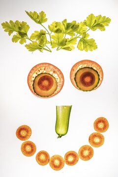 Laughing face of vegetables, smiley face, slices of cucumber, carrot and tomato with parsley, white background, food photography