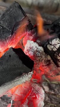 Glowing red embers and burning flames in a barbecue grill getting ready for roasting meat, with hot charcoal, smoke, and ash creating an intense fire background