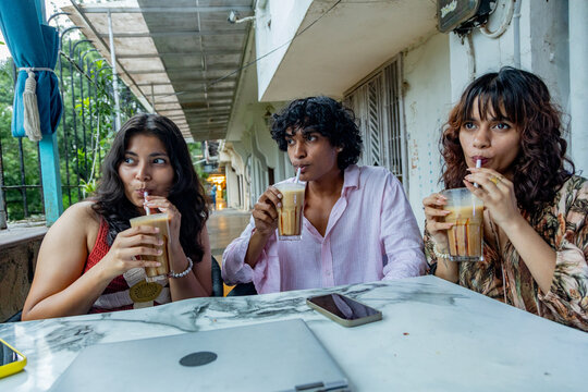 Young indian Gen Z friends enjoy clinking glasses of iced coffee at an outdoor cafe, friendship and social connection.