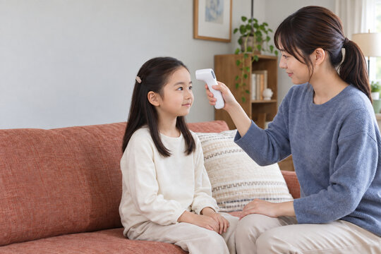 Mother checking daughter's temperature with a noncontact thermometer，自宅で非接触体温計を使い娘の体温を測る母親