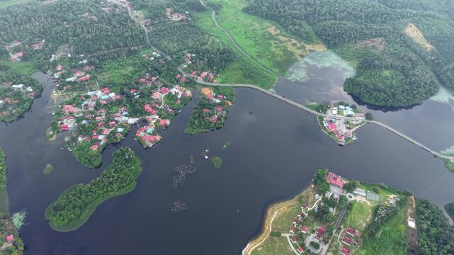 Aerial view showing a wide river surrounded by dense green forest and small residential area connected by a road cutting through the water at Tasik Raban
