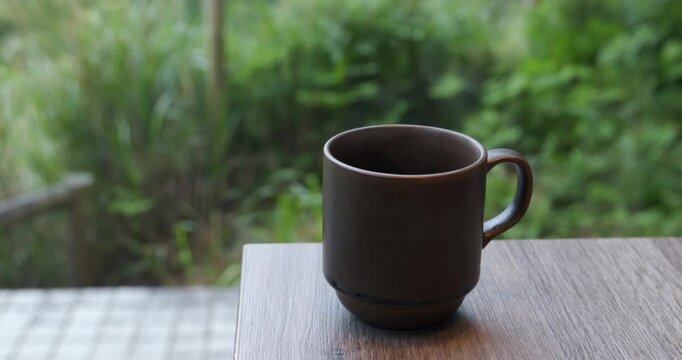 緑豊かな自然を背景に木目テーブルへ置かれたシックなマグカップ